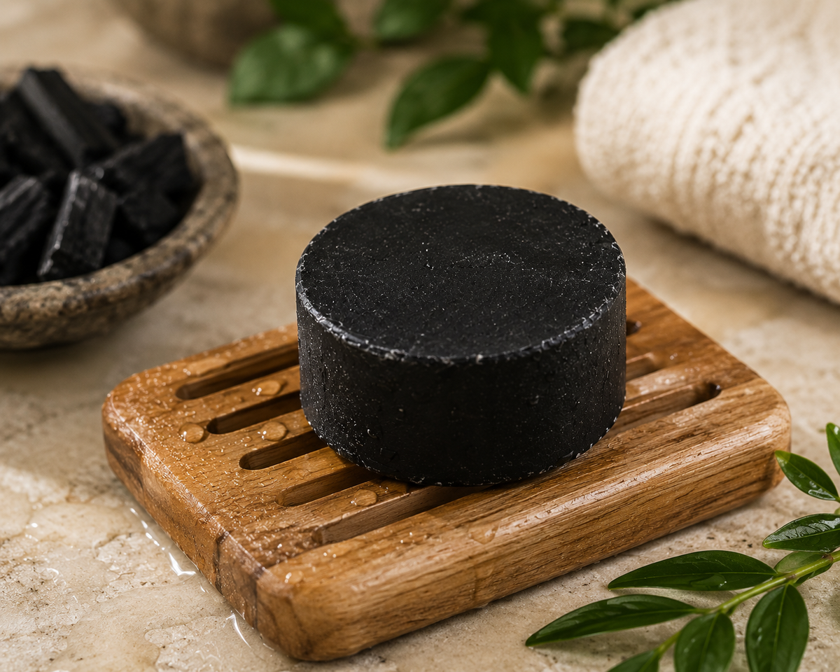 A round black charcoal Nandini ayurvedic soap bar sits on a small wooden soap dish